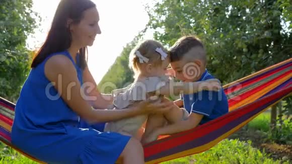 家庭关系和女儿和儿子在一起的快乐女人在丰收的时候在苹果园的吊床上度过时光视频的预览图