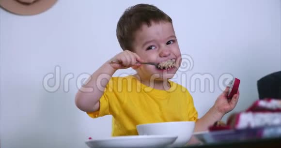 小可爱的孩子坐在桌子旁吃自己的燕麦片吃异国情调的水果宝宝心甘情愿地吃概念视频的预览图