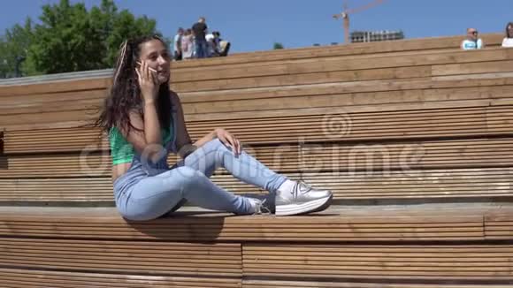 那个女孩坐在公园的长凳上心情很好正在用手机说话4K视频的预览图