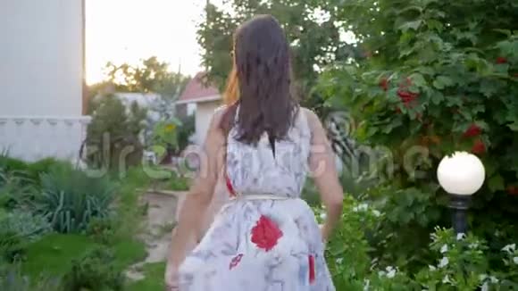 女人的魅力穿着飞天裙的甜美女孩漫步在庭院的树丛中视频的预览图