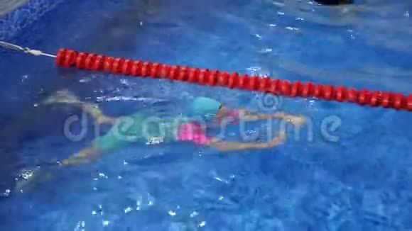 戴着护目镜泳衣帽和脚蹼的小女孩正在游泳池里训练游泳视频的预览图