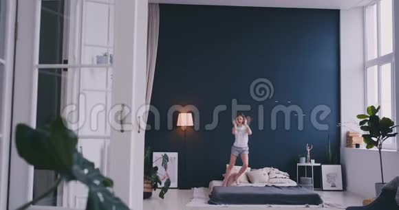 有趣可爱的小女孩戴着无线耳机跳舞梳着梳子唱歌在度假的早晨跳着床视频的预览图