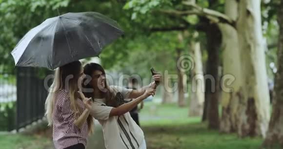 在下雨天微笑着两个年轻的女人在街中央的伞下自拍视频的预览图
