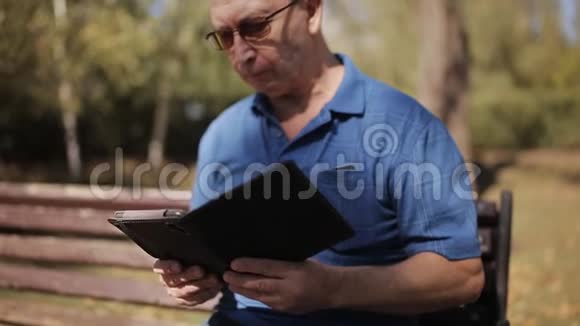 戴眼镜的老人在公园长凳上看电子书视频的预览图