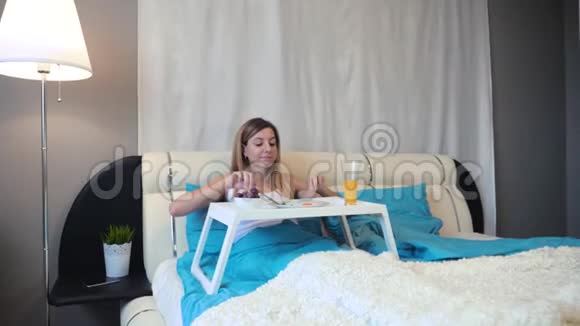 把镜头移向躺在床上的女人她在看台上吃着美味的早餐视频的预览图