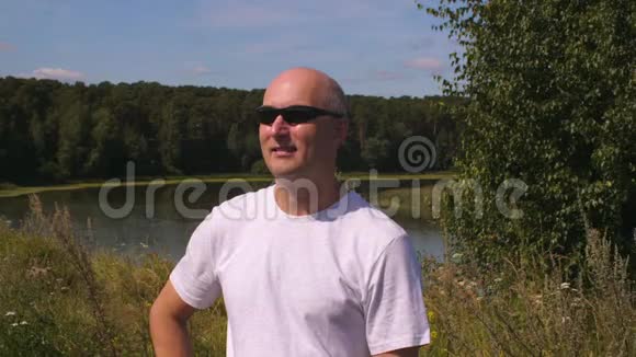 背景绿色森林和湖水中戴太阳镜的成年男子肖像视频的预览图