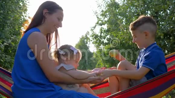 快乐的农村家庭有孩子的女性在丰收的时候坐在苹果园的吊床上玩视频的预览图