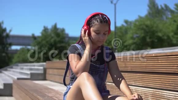 女孩在公园的长凳上听耳机马鞍上的音乐慢动作视频的预览图