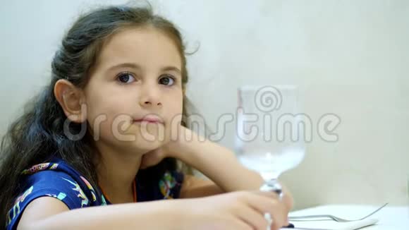肖像特写漂亮的小女孩卷曲的头发深色头发坐在餐厅的桌子旁扭动视频的预览图