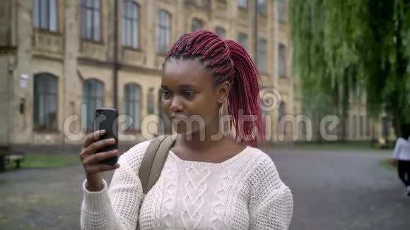 一个年轻的非洲学生带着粉红色的长发通过智能手机进行视频聊天谈笑风生快乐的女人视频的预览图
