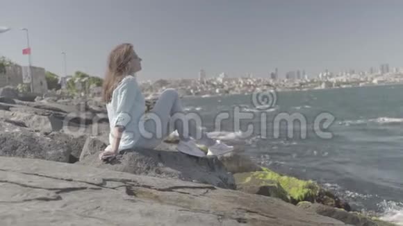 伊斯坦布尔海边的岩石上坐着一位美丽的年轻女子视频的预览图
