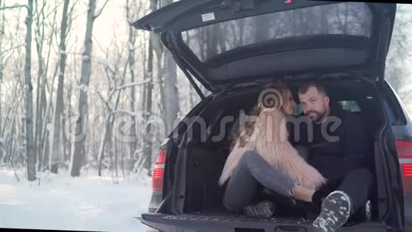 冬天一对年轻夫妇坐在汽车的后备箱里美丽的国际情侣在大自然中放松视频的预览图