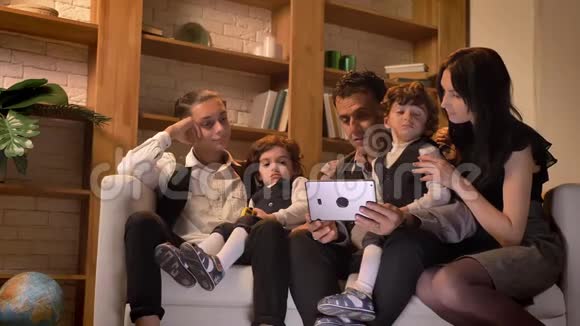 阿拉伯家庭坐在沙发上在舒适的氛围中饶有兴趣地观看客厅里的平板电脑视频的预览图