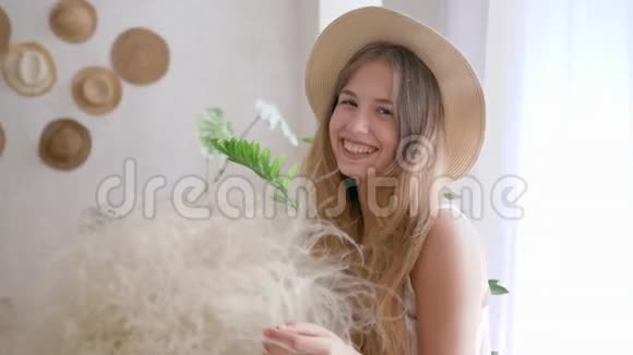 健康的女人戴着草帽的羽毛草微笑着在卧室里看着镜头视频的预览图