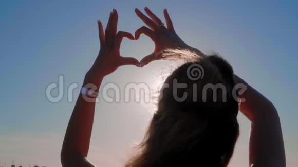 这个女孩用双手在海的背景上做心脏剪影手在心形与日落里面假期视频的预览图