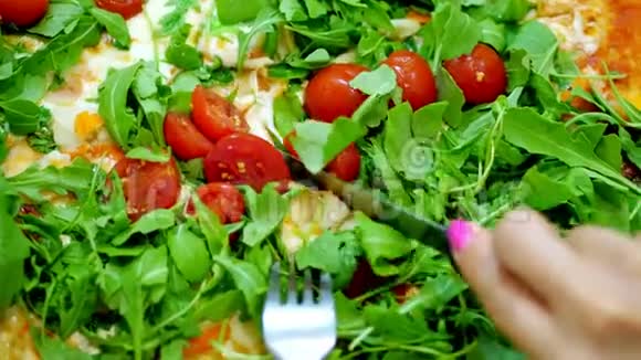 特写大的多汁热的比萨饼与绿色木耳和樱桃番茄女人用刀叉切披萨视频的预览图