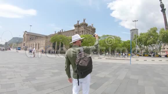 一个年轻人游客背着背包戴着帽子在哥伦布纪念碑附近用智能手机拍照视频的预览图