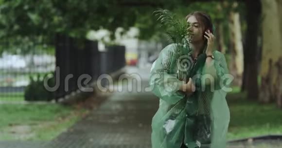 特写美女带着一朵花在下雨天走在街上听着耳机里的音乐视频的预览图