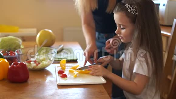 可爱的长发女孩在厨房里切甜椒她的母亲专心地看着她的女儿女童教育视频的预览图