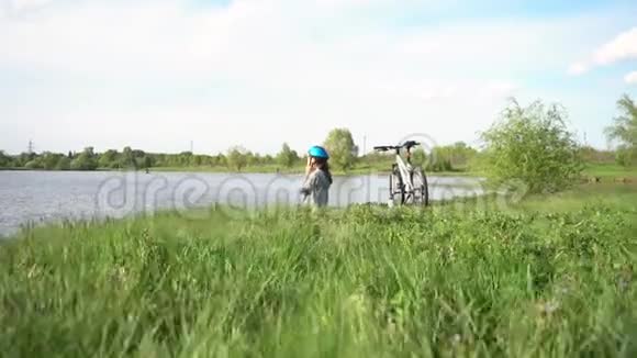 年轻女子骑着自行车在湖或河的背景下穿过公园视频的预览图