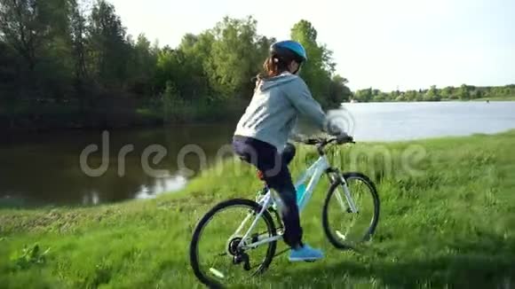 年轻女子骑着自行车在湖或河的背景下穿过公园视频的预览图
