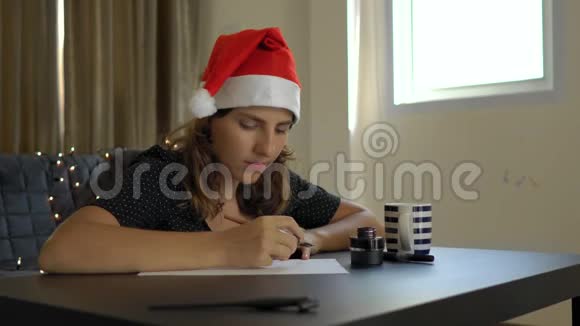 用刻字技术在一张纸上写圣诞帽书法的年轻女子特写镜头她写字视频的预览图