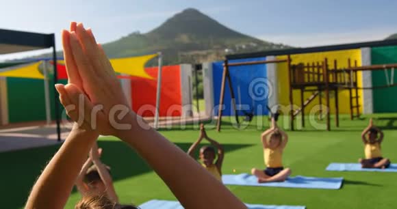女教师教学童在学校操场练习瑜伽的后视图视频的预览图