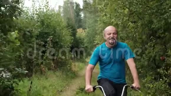 穿着蓝色t恤的高白种人男性在树间骑着自行车在户外度假视频的预览图