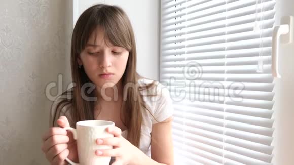 伤心的女孩喝茶坐在窗台上女孩手里拿着白色的玻璃看着窗外视频的预览图