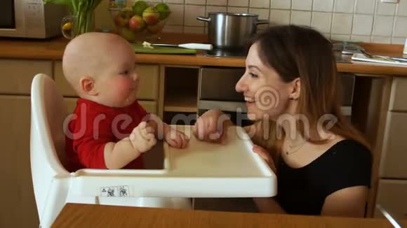 小妈妈带着孩子在厨房一个女人坐在高椅上喂婴儿生菜叶视频的预览图