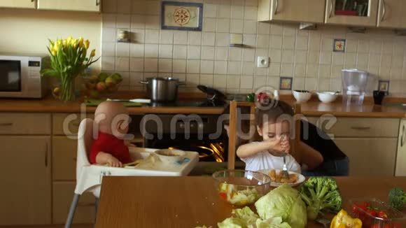 厨房里的一个保姆用午餐和准备晚餐喂两个孩子工程处本国工作人员视频的预览图