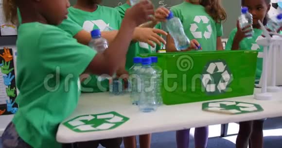 混合种族的学龄儿童在4k教室的托盘中放置回收瓶视频的预览图