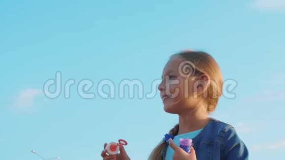 在蓝天背景下吹肥皂泡的人像女孩低角度视角视频的预览图