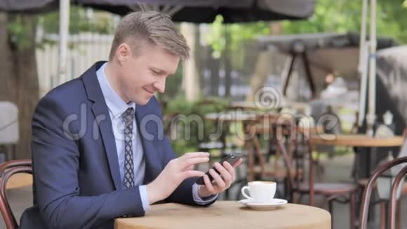 使用智能手机的商人坐在户外咖啡厅视频的预览图