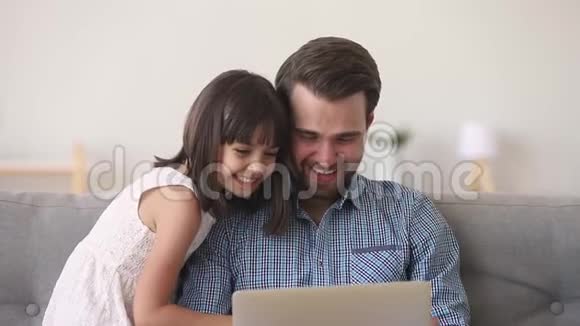 快乐的爸爸和可爱的小女儿在笔记本电脑上看动画片视频的预览图