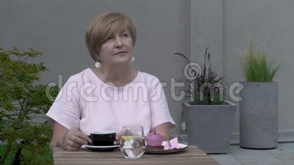 一位坐在露台上的漂亮老妇人的特写她一个人喝茶反映视频的预览图