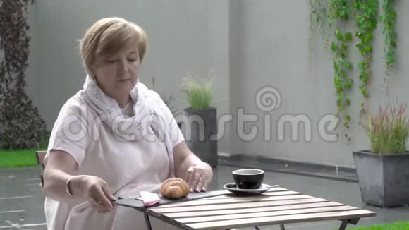 一位美丽的老妇人正在吃一个羊角面包她坐在外面的露台上视频的预览图