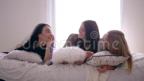 快乐的朋友女孩八卦在睡眠聚会上玩得开心躺在家里有枕头的床上视频的预览图