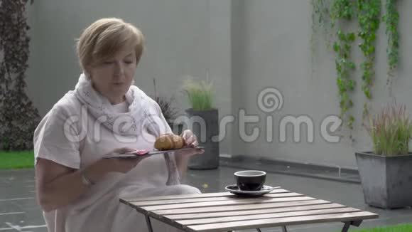 一位漂亮的老妇人正在吃羊角面包和喝茶她坐在露台上视频的预览图
