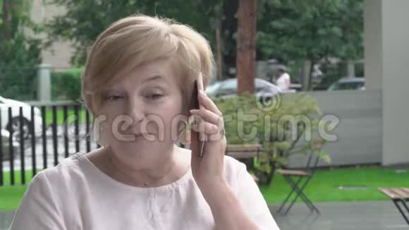 一个漂亮的老妇人在电话里说话的特写她坐在外面的露台上视频的预览图