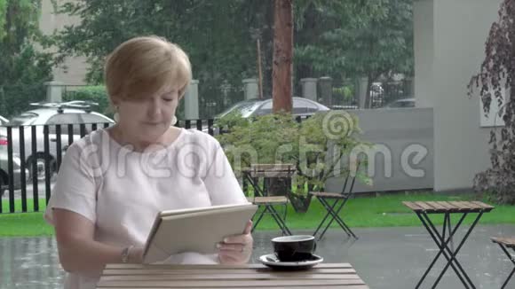 在露台上一位年迈的妇女一边喝着咖啡一边看着平板电脑对新闻的反应视频的预览图
