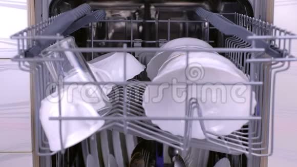男人在洗碗机里装满脏的白色盘子把篮子推到里面并关上视频的预览图