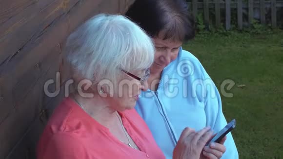 两位老妇人一起在乡村花园里浏览手机视频的预览图