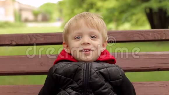 公园里一个快乐的笑男孩在长凳上的特写肖像视频的预览图