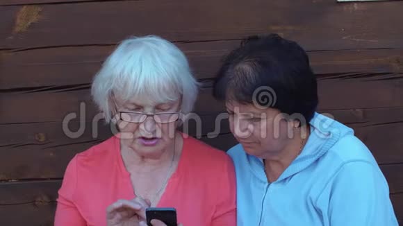 两个年长的女人一起看智能手机在户外聊天视频的预览图