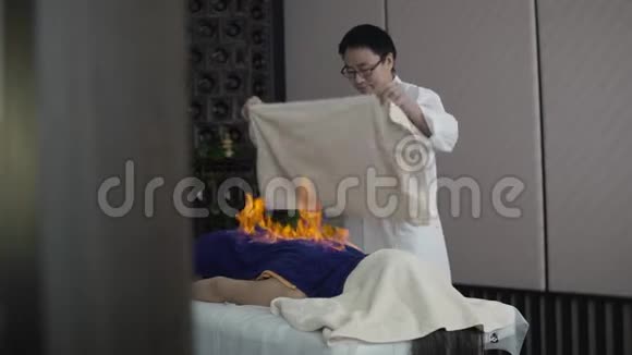 一名亚洲男子在中国的一次消防按摩中向躺在毛巾下的人灭火视频的预览图