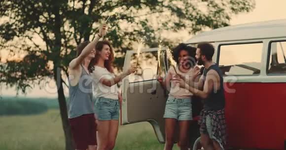 在野餐时和朋友们跳舞手里拿着一个闪闪发光的东西在他们的老式货车旁边享受着时光视频的预览图