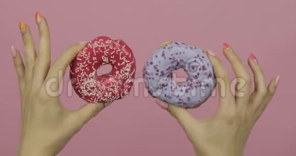 女人的手拿着两个红色和蓝色洒在粉红色背景上的甜甜圈视频的预览图
