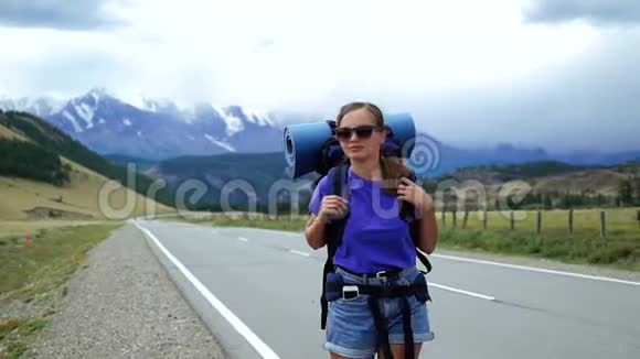 年轻的旅游妇女带着背包和太阳镜走在山路上然后她停下来拿视频的预览图