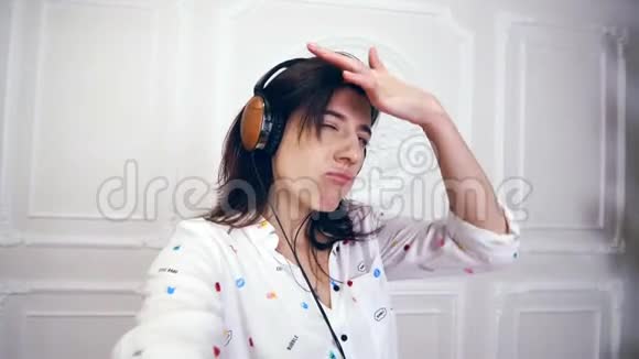 有趣的年轻女人的肖像女孩黑发穿着白色衬衫戴着耳机她听音乐拍摄视频视频的预览图